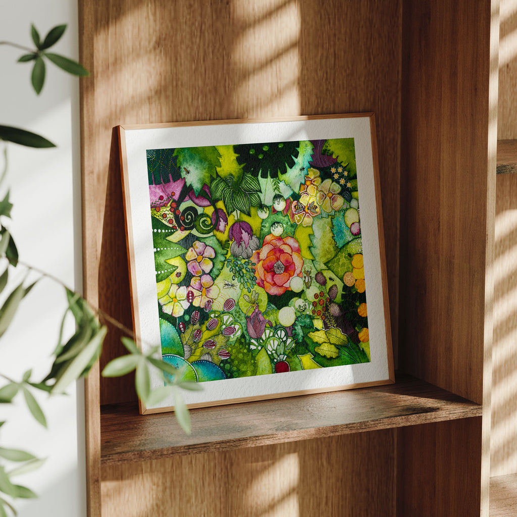 Framed Green Lush fine art print leaning on a wooden shelf in dappled daylight, a lush watercolour thicket with a central coral rose, flowers and hidden insects, from Léna Ruisz's Cabinet of Small Worlds collection.