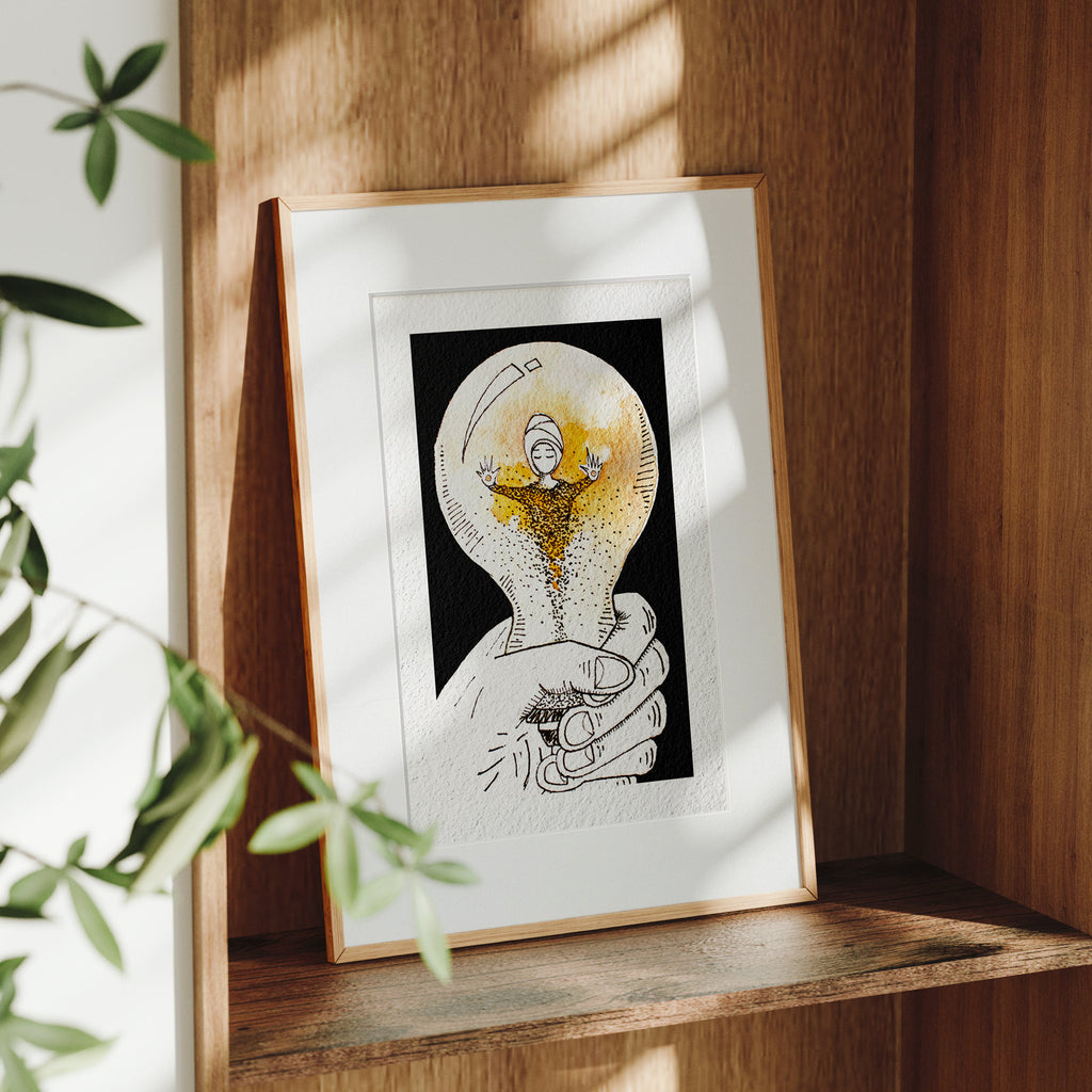 Framed Held fine art print on a wooden shelf in dappled daylight, cupped hands holding a glowing orb where a turbaned figure dissolves into falling particles, by Léna Ruisz.