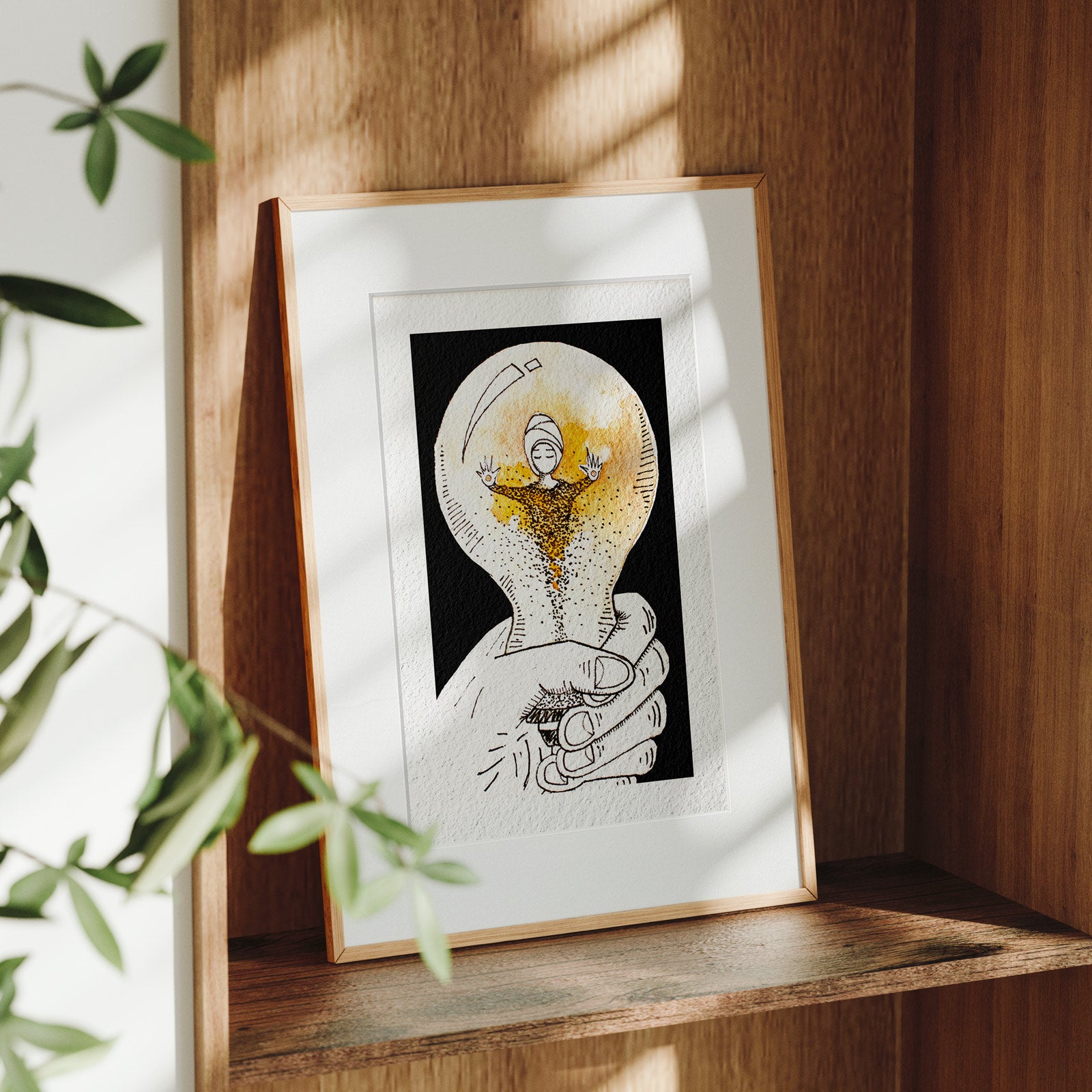 Framed Held fine art print on a wooden shelf in dappled daylight, cupped hands holding a glowing orb where a turbaned figure dissolves into falling particles, by Léna Ruisz.