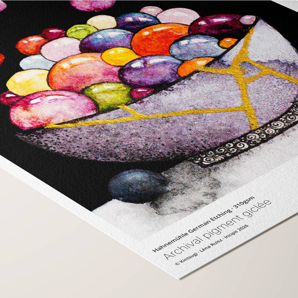 Corner of the Kintsugi fine art print on Hahnemühle German Etching paper, a gold-repaired bowl overflowing with glossy coloured spheres on black, angled to show paper texture and printed credentials.
