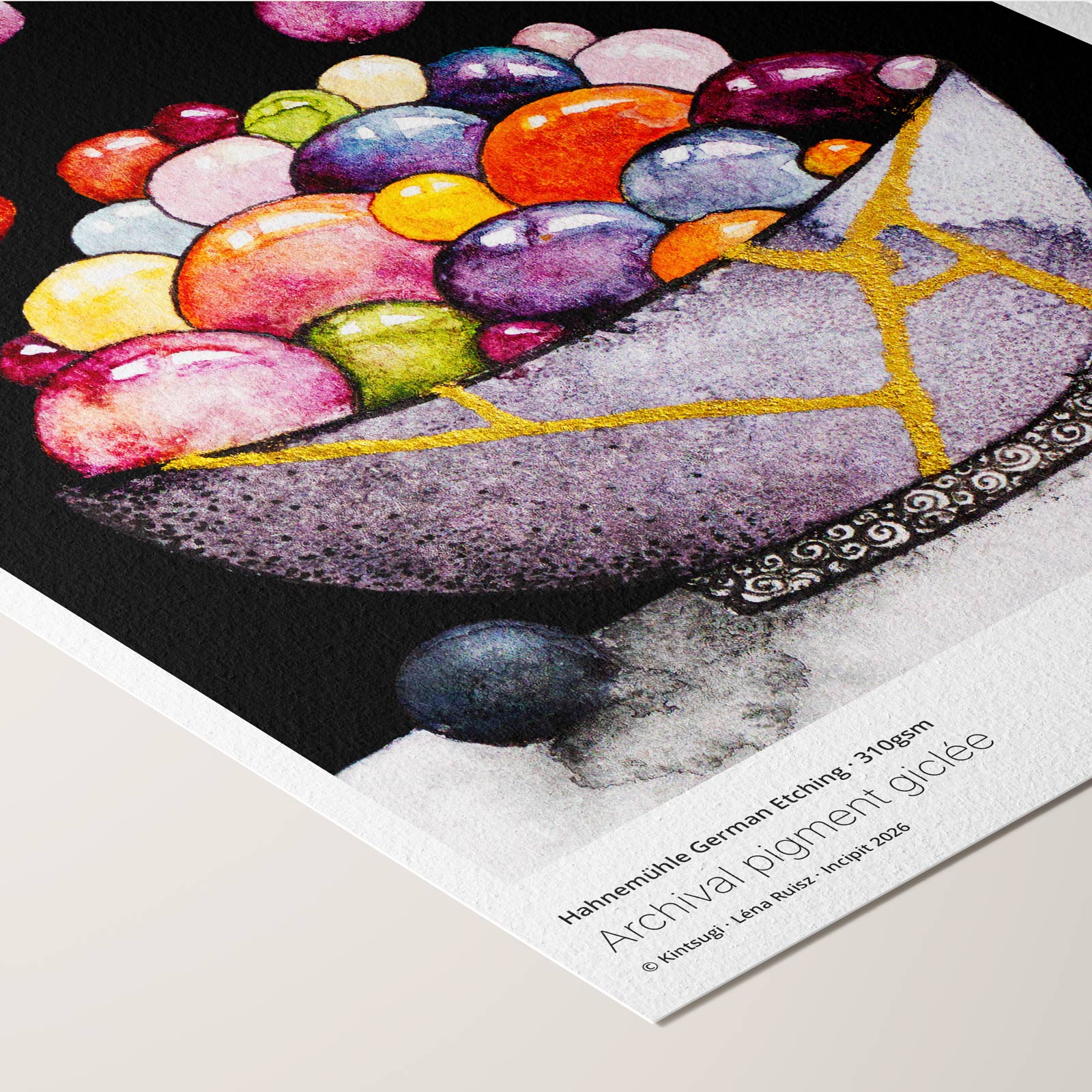 Corner of the Kintsugi fine art print on Hahnemühle German Etching paper, a gold-repaired bowl overflowing with glossy coloured spheres on black, angled to show paper texture and printed credentials.
