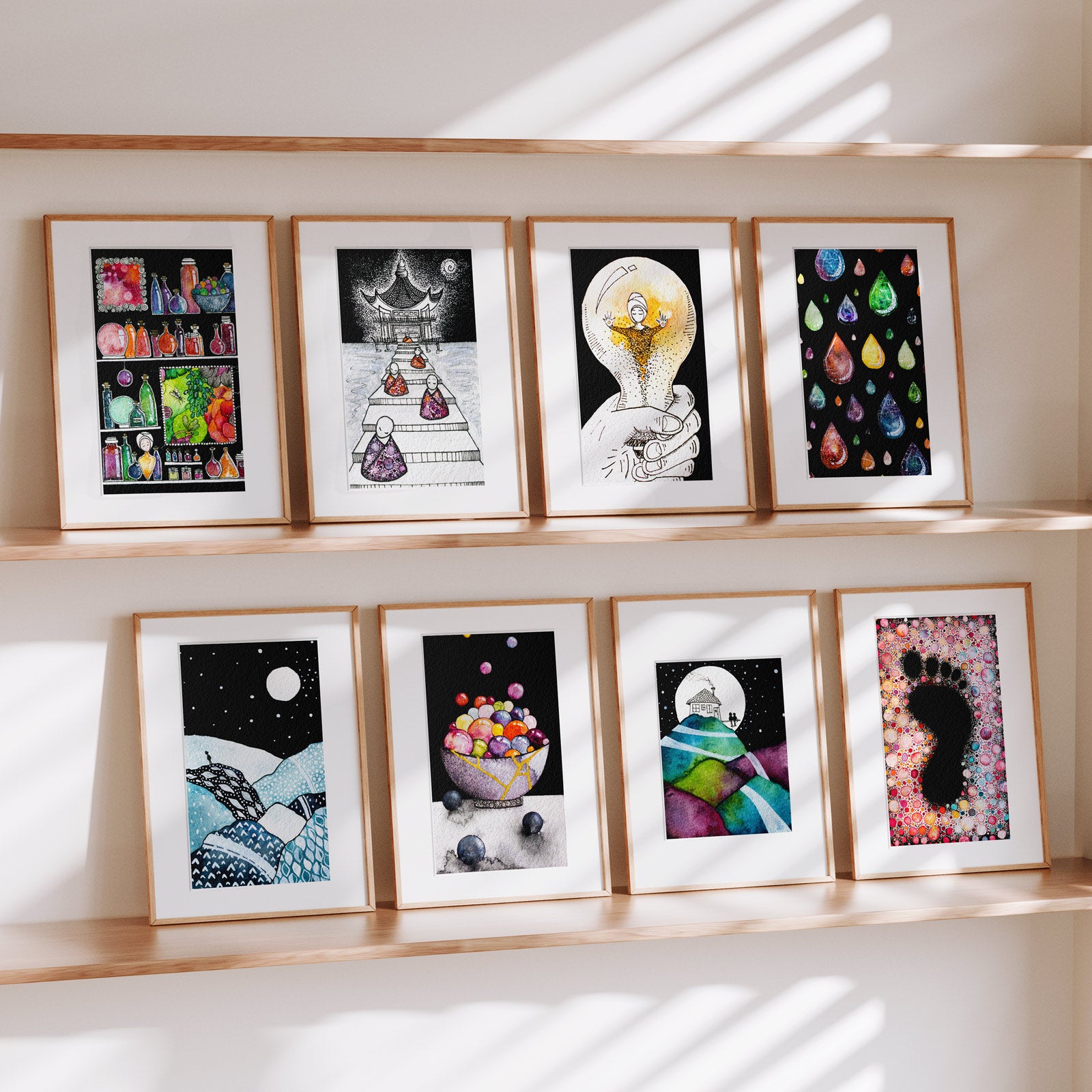 Eight framed Small Narratives fine art prints on wooden ledges in soft daylight, intimate watercolour and ink scenes including a moonlit hilltop house, a temple stairway, a gold-repaired bowl and a footprint of colour, by Léna Ruisz.