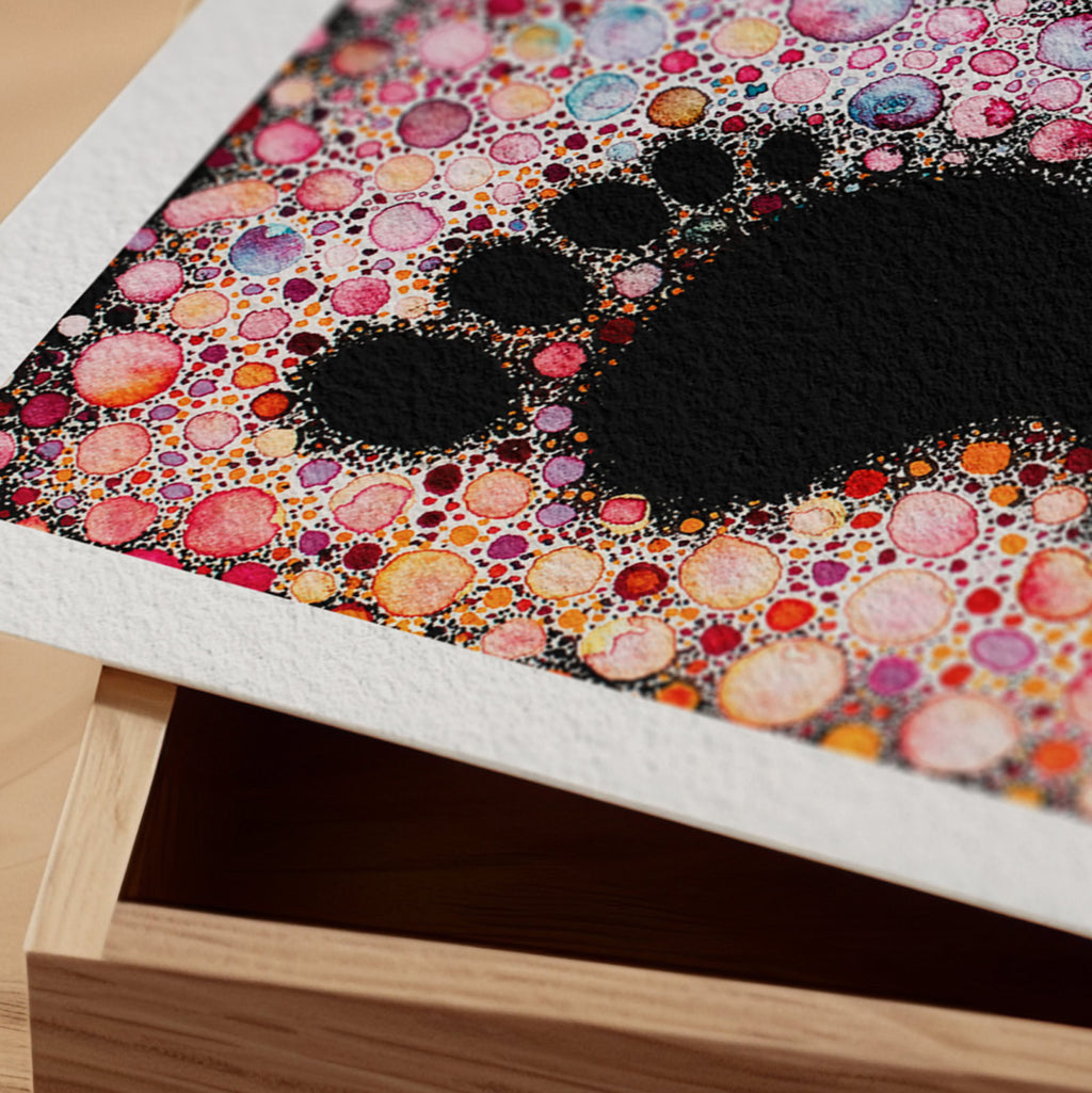 Detail of the Spoor fine art print resting on a wood surface, showing the deckle paper edge and close-up of a footprint formed in black negative space within a field of stippled jewel-toned dots in watercolour and ink