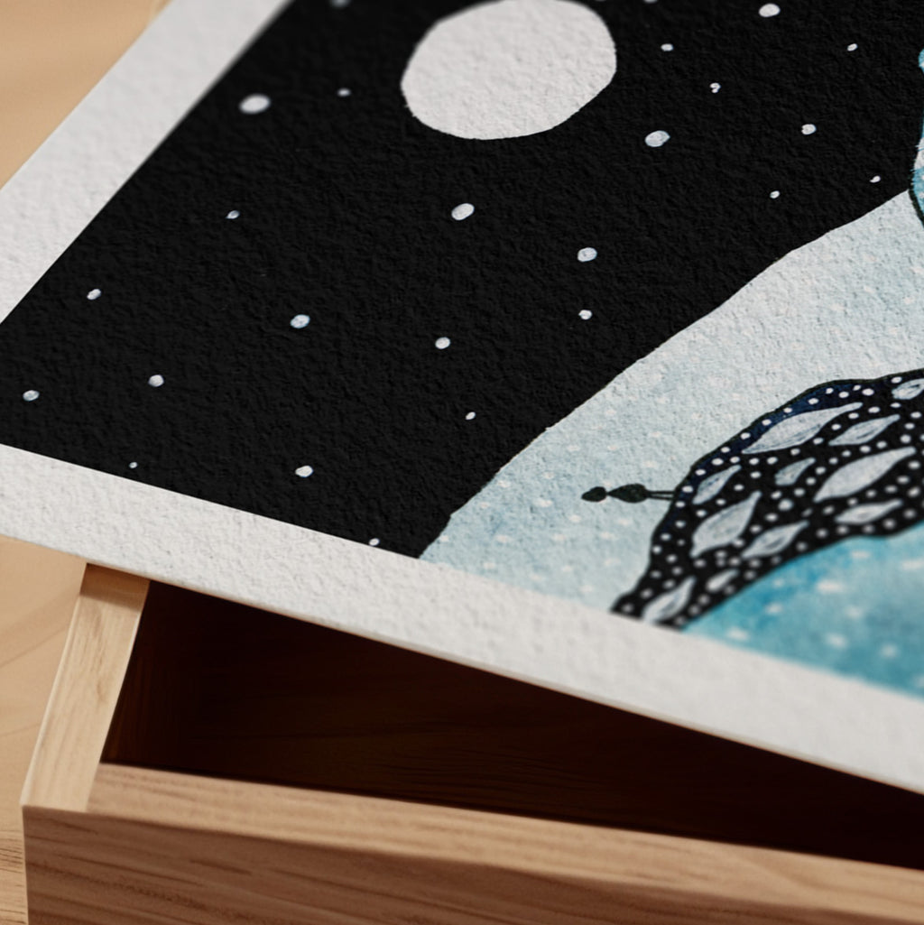Detail of The Watcher fine art print resting on a wood surface, showing the deckle paper edge and close-up of a full moon over a starrynight sky with a patterned dark creature in ink and watercolour